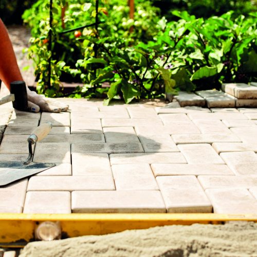 The master lays paving stones in layers. Garden brick pathway paving by professional paver worker. Laying gray concrete paving slabs in house courtyard on sand foundation base.
